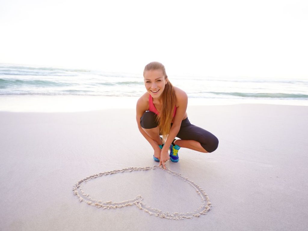 woman drawing heart in sand